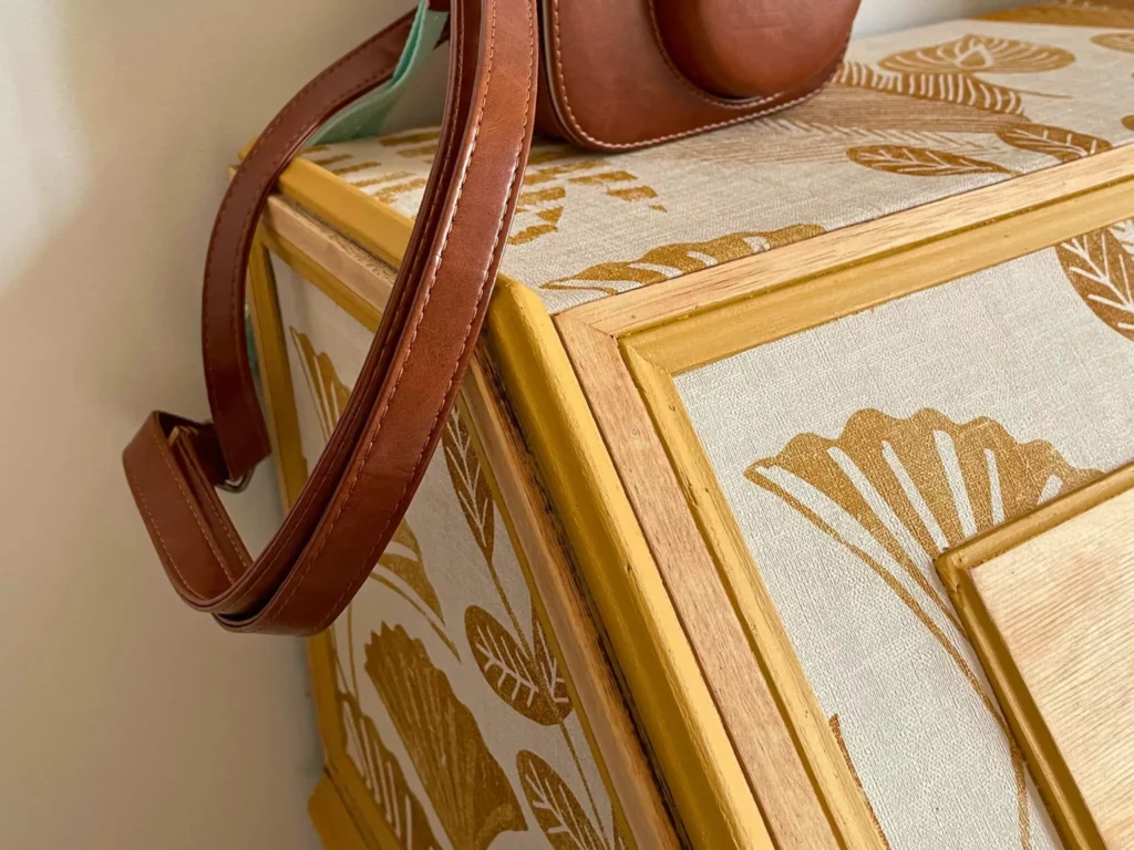 Détail d'un meuble rénové recouvert de papier peint et peinture ocre pour être assorti au reste de la décoration de la chambre.