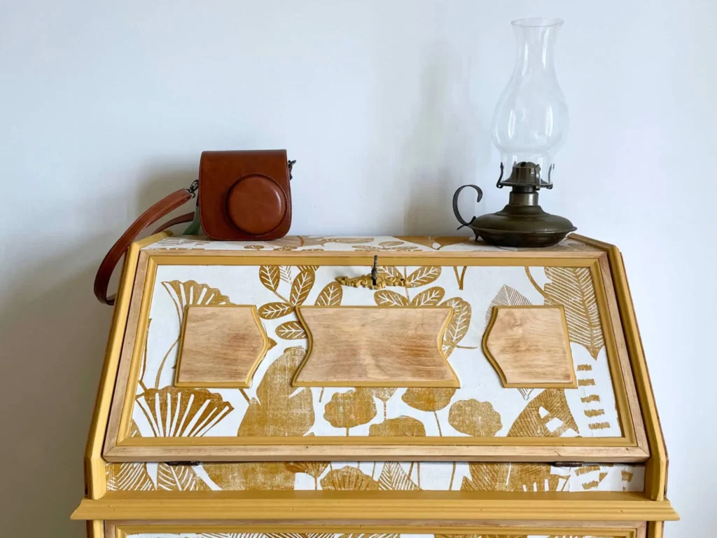 Détail d'un meuble rénové recouvert de papier peint et peinture ocre pour être assorti au reste de la décoration de la chambre.